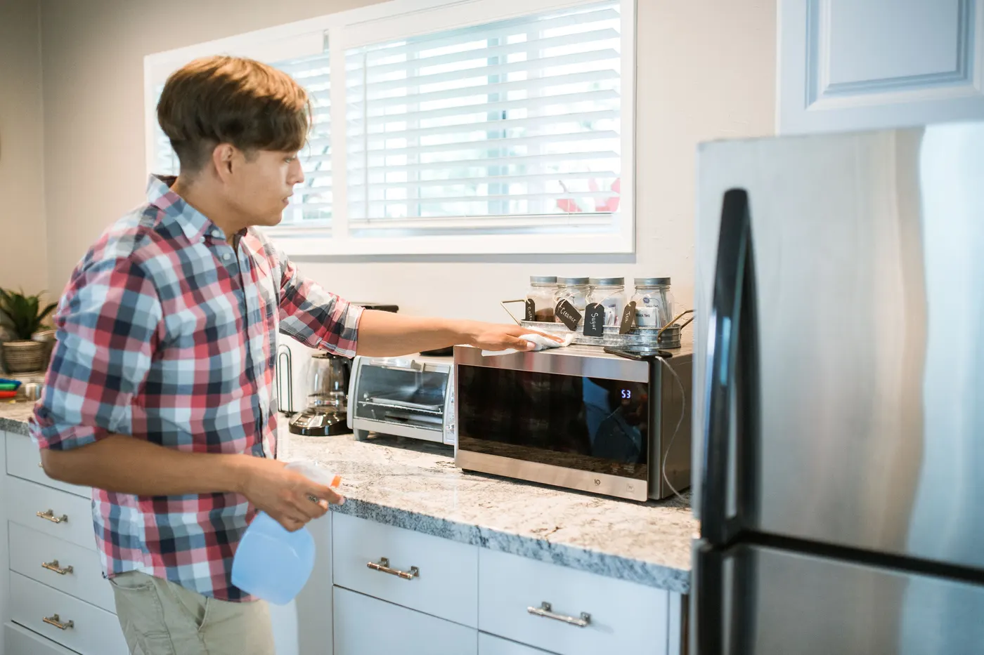 Stock photo of a man wiping down a kitchen counter next to the microwave